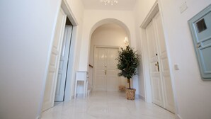Un couloir aux murs blancs, une porte blanche au fond, et un lustre.