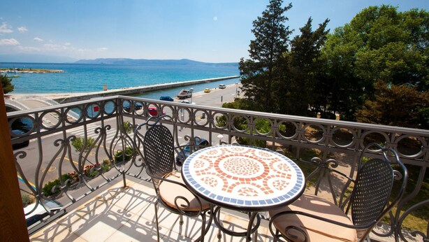 Un balcon doté d’une table et de chaises, offrant une vue dégagée sur la côte, la mer et les montagnes lointaines.