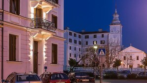 Un immeuble à plusieurs étages doté de balcons, avec des voitures garées et un beffroi en arrière-plan.