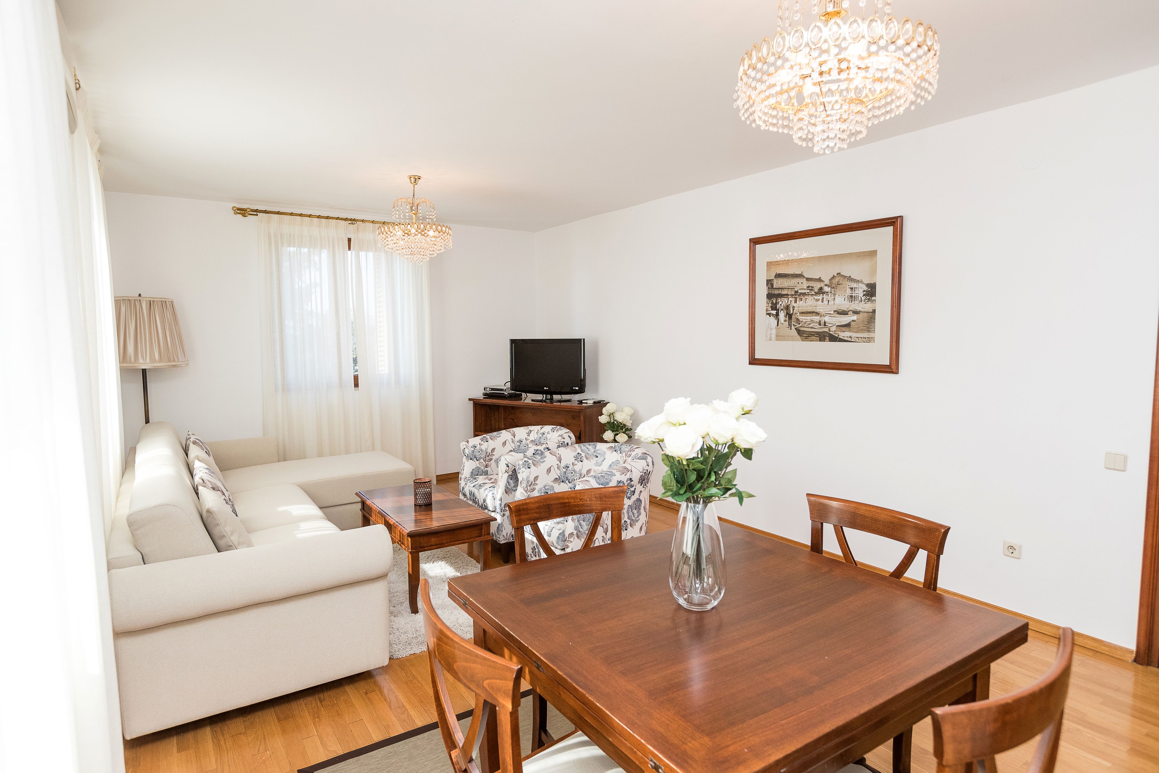 A living room with a sofa, a dining table with chairs, a TV, and a chandelier.