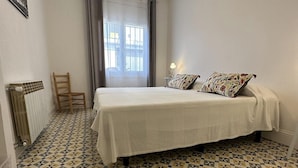 Ein Schlafzimmer mit Bett, Sessel, Heizkörper und einem fenster mit Vorhängen.