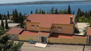 A two-story building with a red-tiled roof, a gated entrance, and a view of a large body of water. - Apartments Casa Mia (Crikvenica)