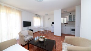 A living room with a sofa, a coffee table, and a TV. There is a dining area with a table and chairs. The kitchen is visible in the background. - Apartments Casa Mia (Crikvenica)