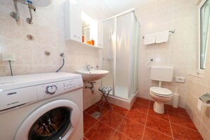 Ein Badezimmer mit Waschmaschine, Waschbecken, Toilette und Duschbereich.