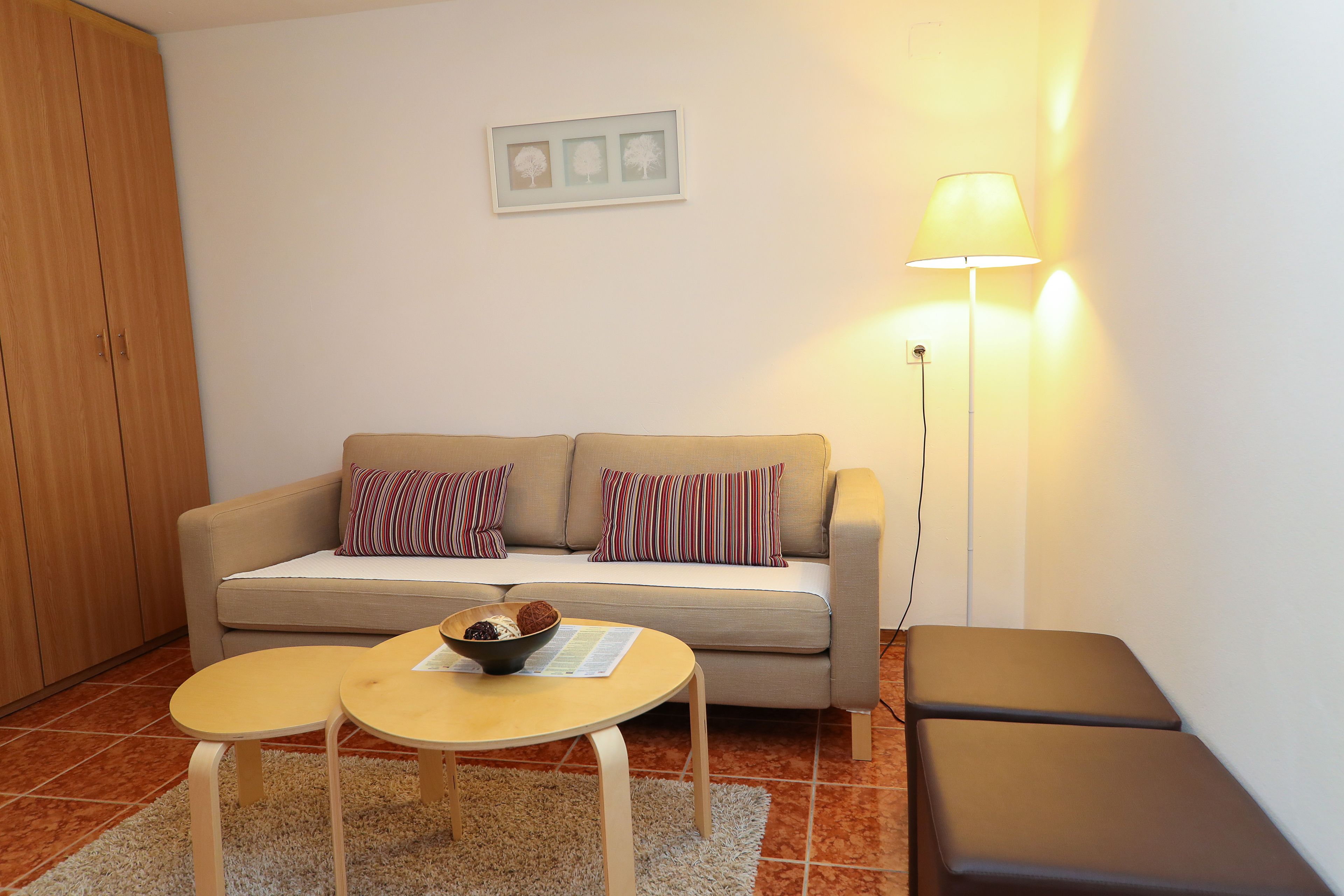 A living room with a sofa, two small tables, a lamp, and a cabinet.