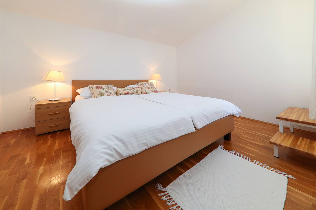 Een slaapkamer met een bed, nachtkastjes, een houten bankje en een vloerkleed.