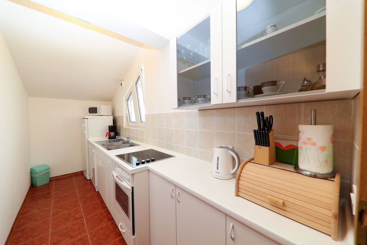 Een kleine keuken met witte kastjes, een magnetron, een fornuis en een spoelbak.