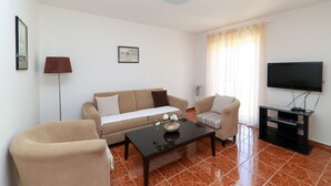 A living room with a sofa, two armchairs, a coffee table, a TV, and a lamp. - Apartments Casa Mia (Crikvenica)
