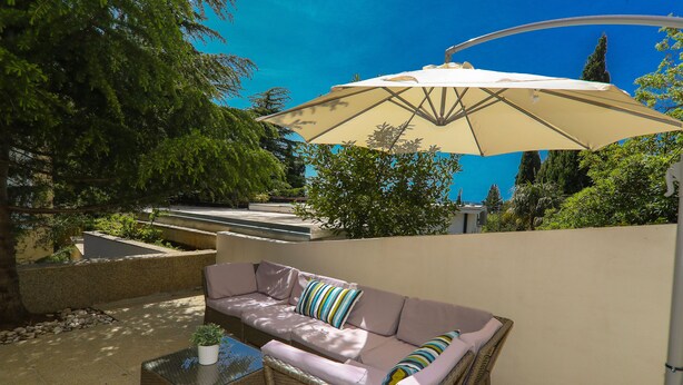 A patio with a wicker sofa, a glass table, and a beige umbrella. - Apartments Casa Mia (Crikvenica)