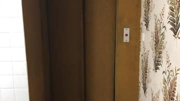 Un ascenseur étroit avec une porte marron, un interrupteur sur le mur et un papier peint à motifs sur le mur adjacent.
