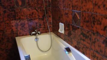 Une salle de bain avec une baignoire blanche, une douchette et une fenêtre au-dessus du lavabo.