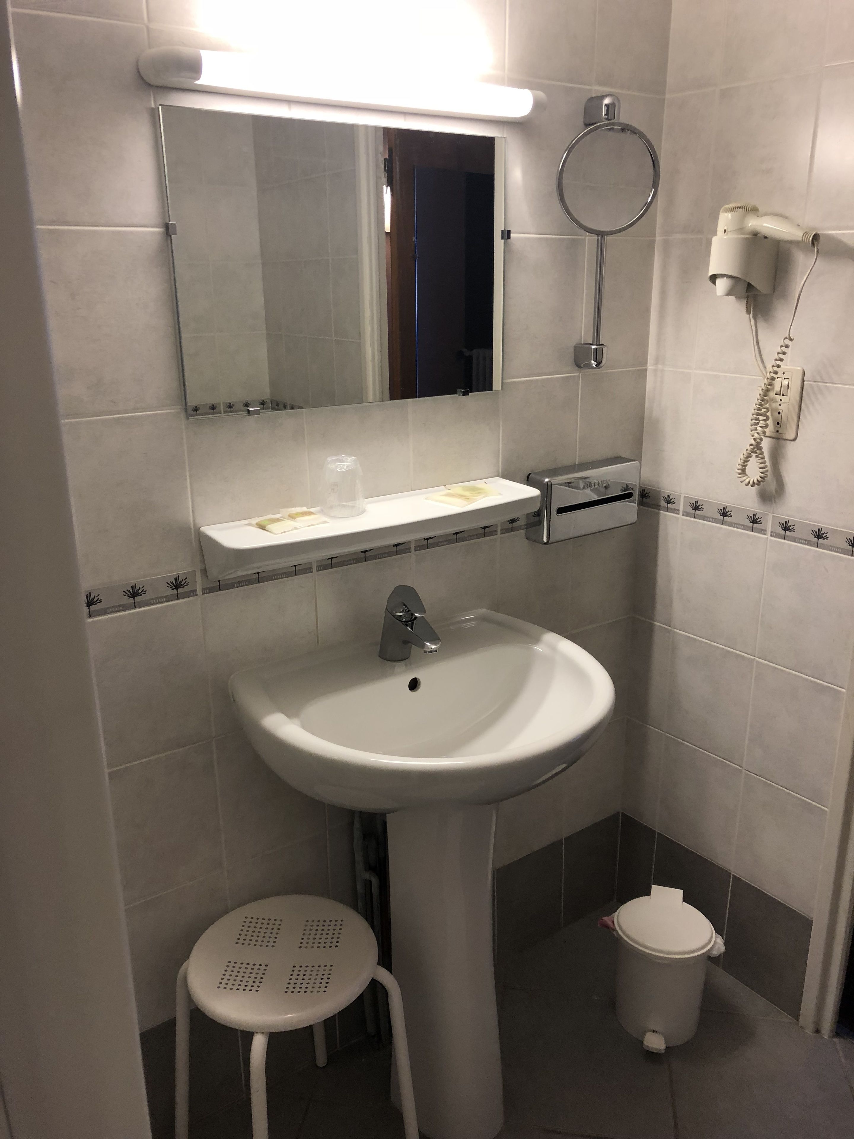 Un baño con lavamanos, espejo, perchero para toallas y un taburete pequeño.