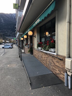 A hotel with a green awning, outdoor seating with red flowers, and a manhole cover on the sidewalk.