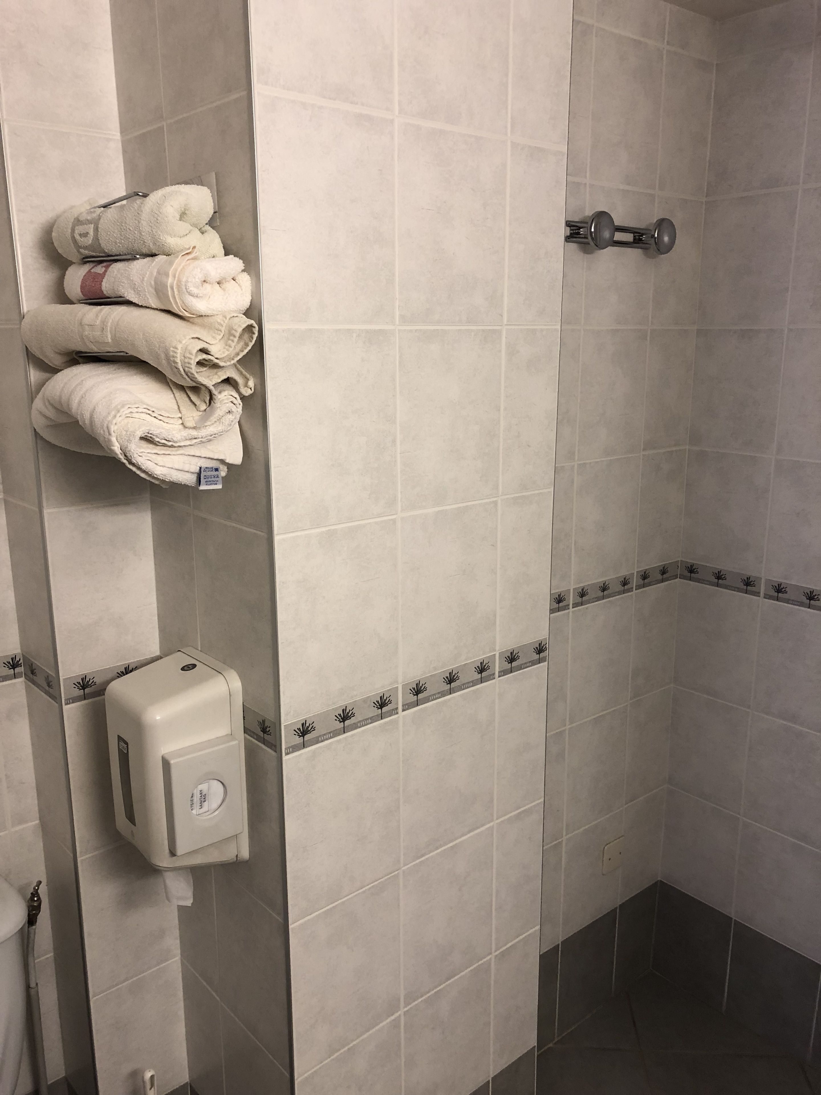 A bathroom with a hand dryer, a towel rack with folded towels, and a shower area with tiled walls.