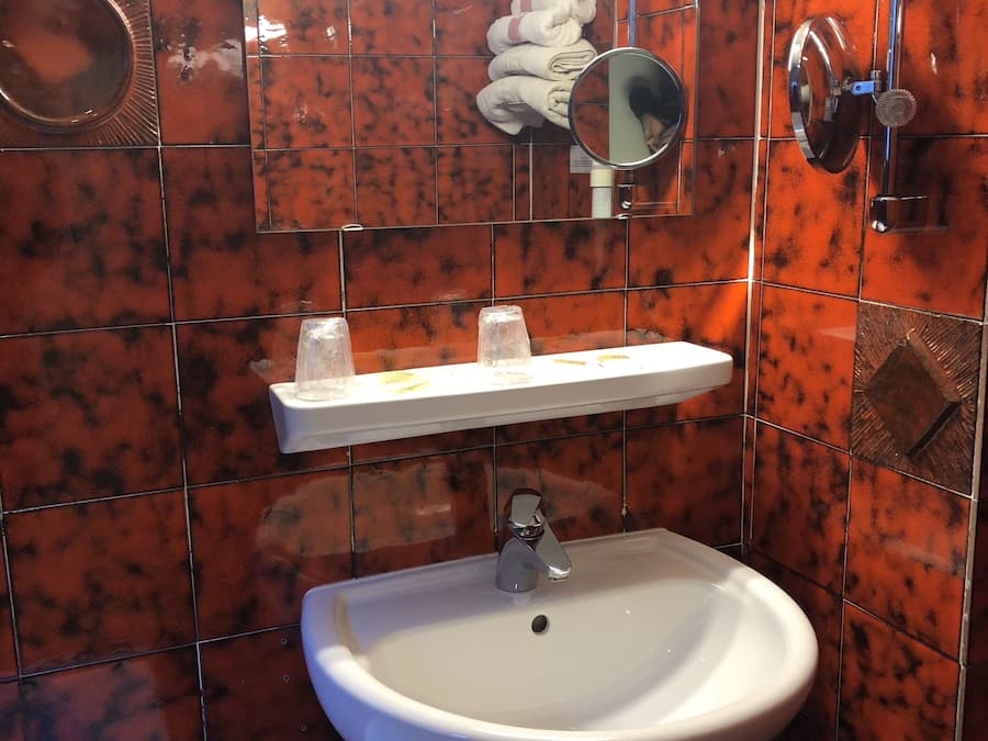 Un baño con un lavamanos blanco de pedestal, un espejo encima y un perchero con toallas dobladas.
