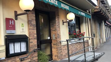 A hotel named "Le Perce Neige" with a brick facade, a green awning, and a small outdoor seating area with a metal railing.