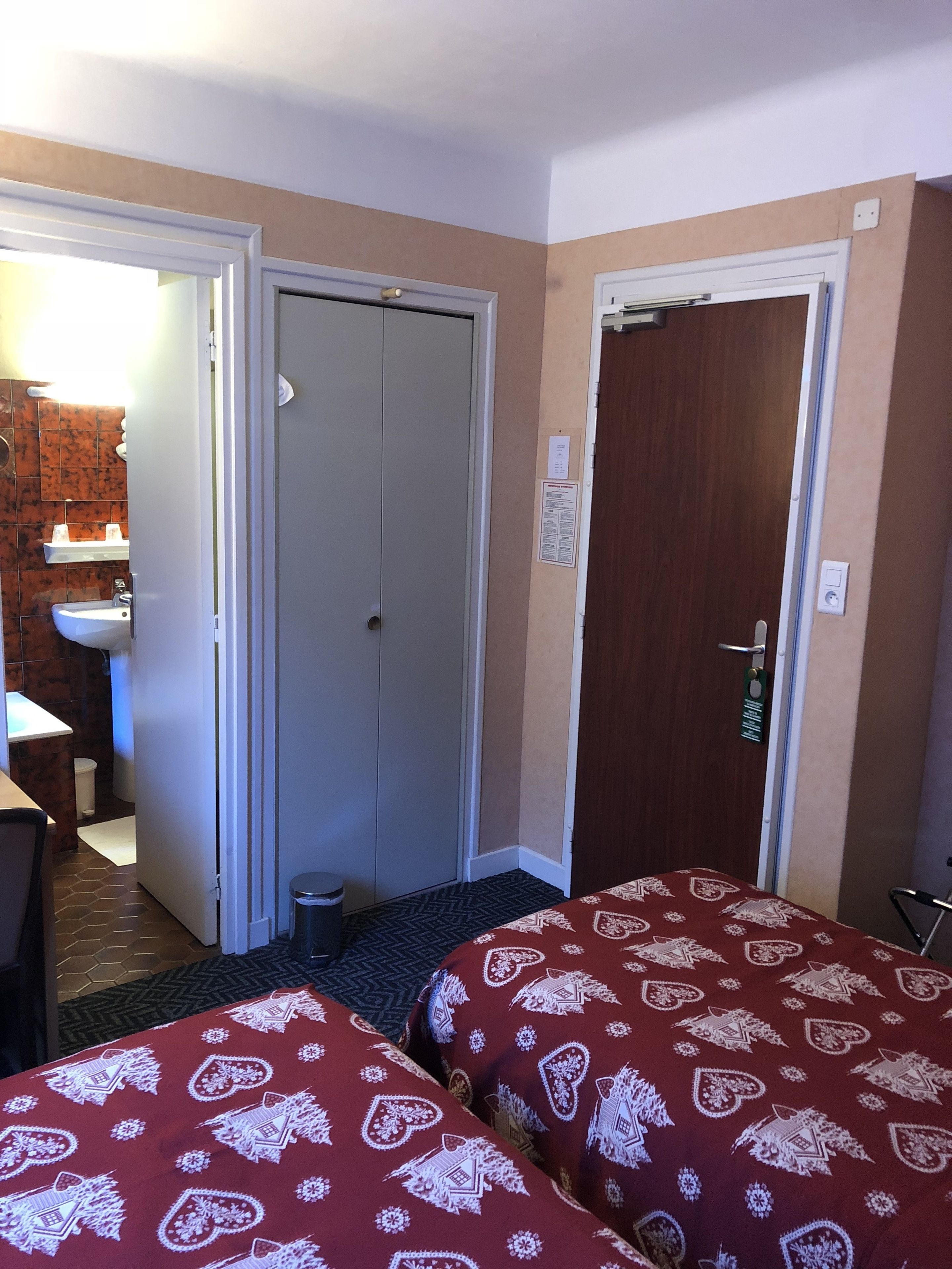 Habitación de hotel con dos camas, un baño con lavamanos y una puerta a otra habitación.