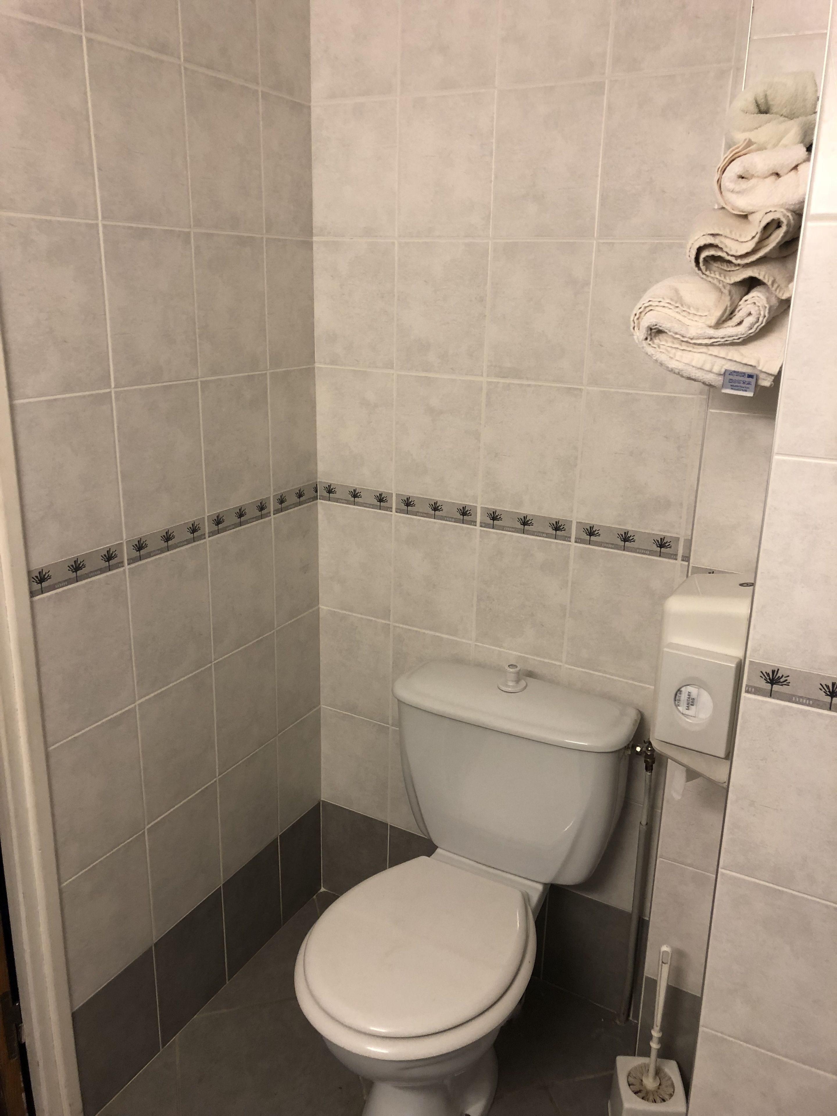 Un baño pequeño con azulejos, un inodoro, un secador de manos y un cepillo para el inodoro.