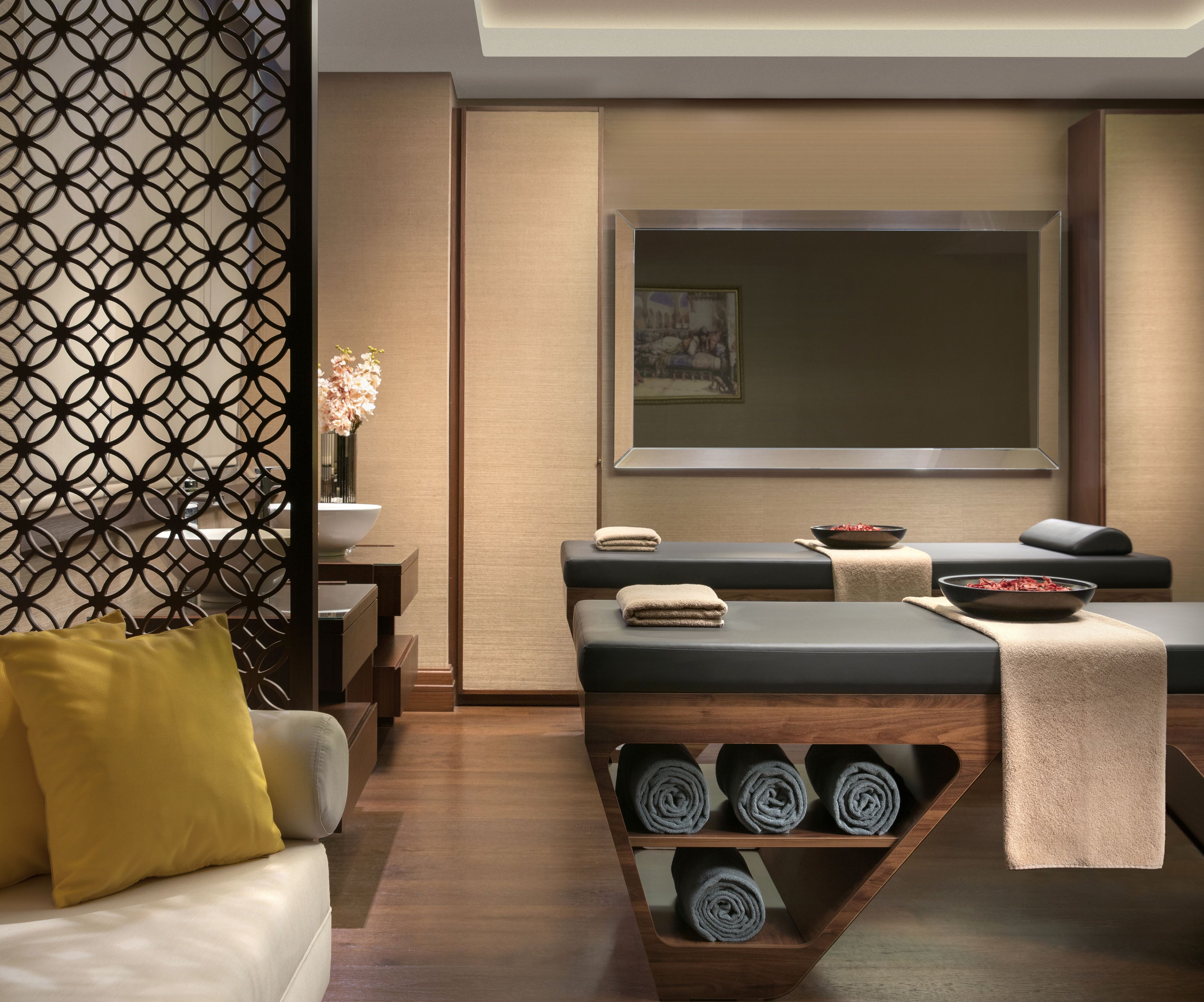 A modern spa room with a massage table, a wooden shelf with towels, and a decorative wall panel.