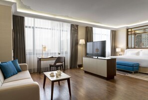 Una habitación de hotel con cama, televisor, escritorio con silla, mesa de centro y sofá.