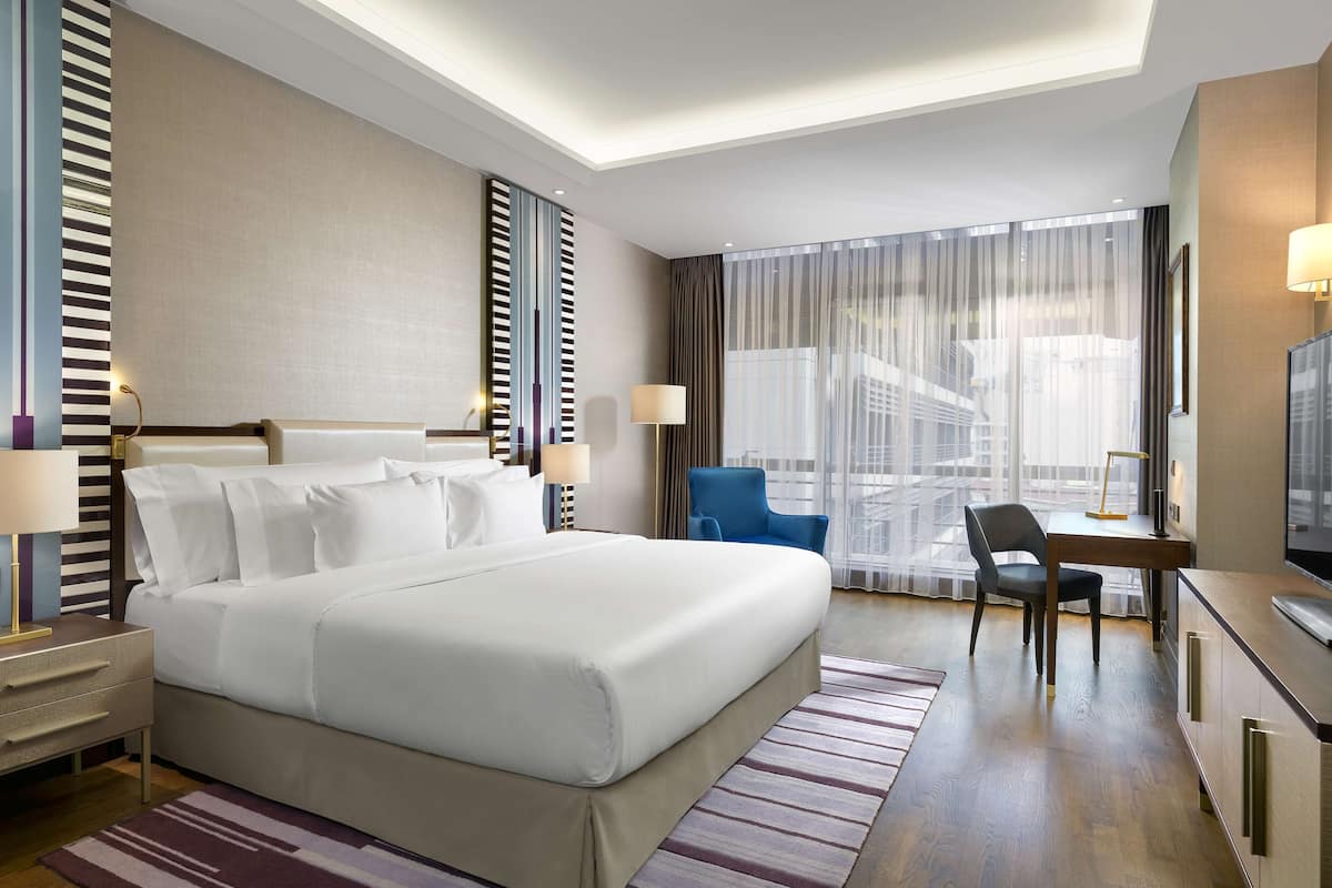 A hotel room with a large bed, a desk, a chair, and a television.