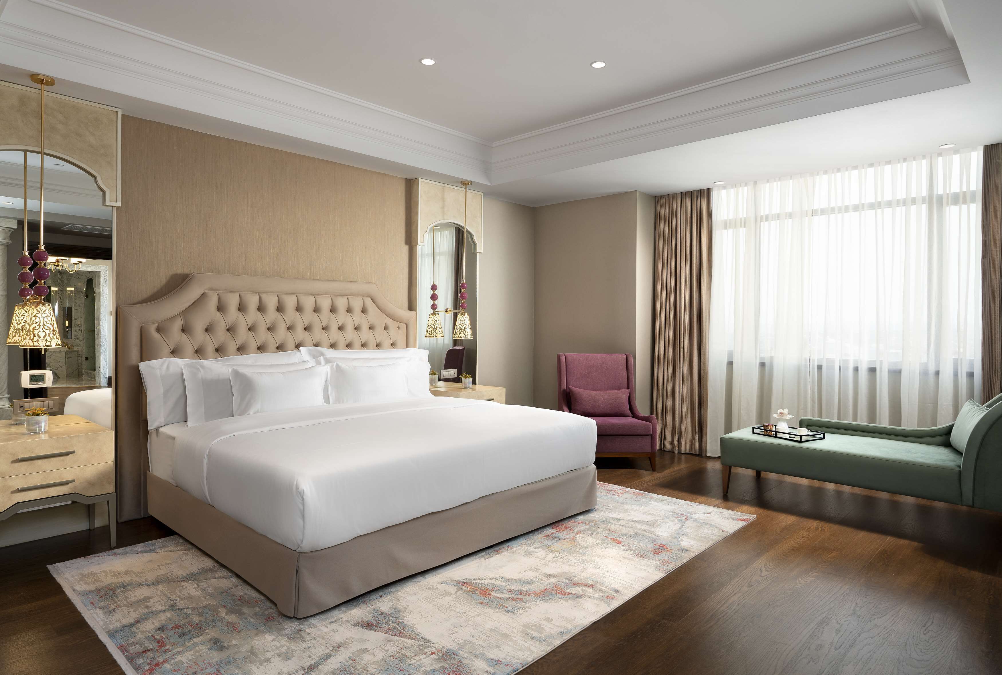 A spacious bedroom with a large bed, a sitting area with a sofa, a chair, and a mirror.