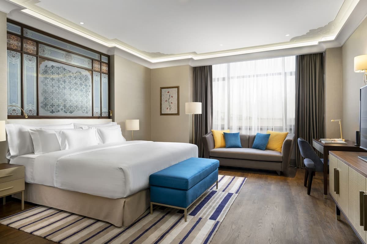 A hotel room with a large bed, a sofa, a desk, and a TV.