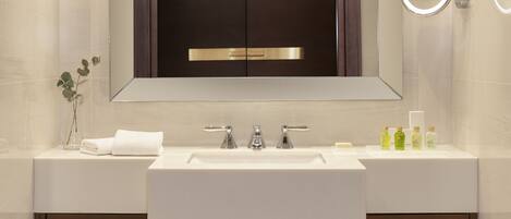 A modern bathroom with a large mirror, two sinks, and a vanity with shelves holding towels.