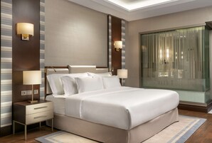 A modern hotel room with a large bed, bedside lamps, a nightstand, and a glass partition wall.