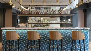 A bar area with a marble countertop, multiple bottles of liquor, and three bar stools.