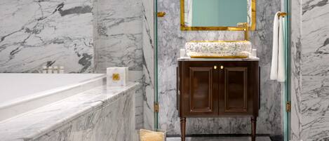 A marble bathroom with a bathtub, a vanity with a mirror, and a glass jar with toiletries.