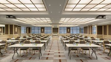 Un salón de conferencias amplio con varias mesas y sillas dispuestas en filas, techo alto y ventanas grandes.