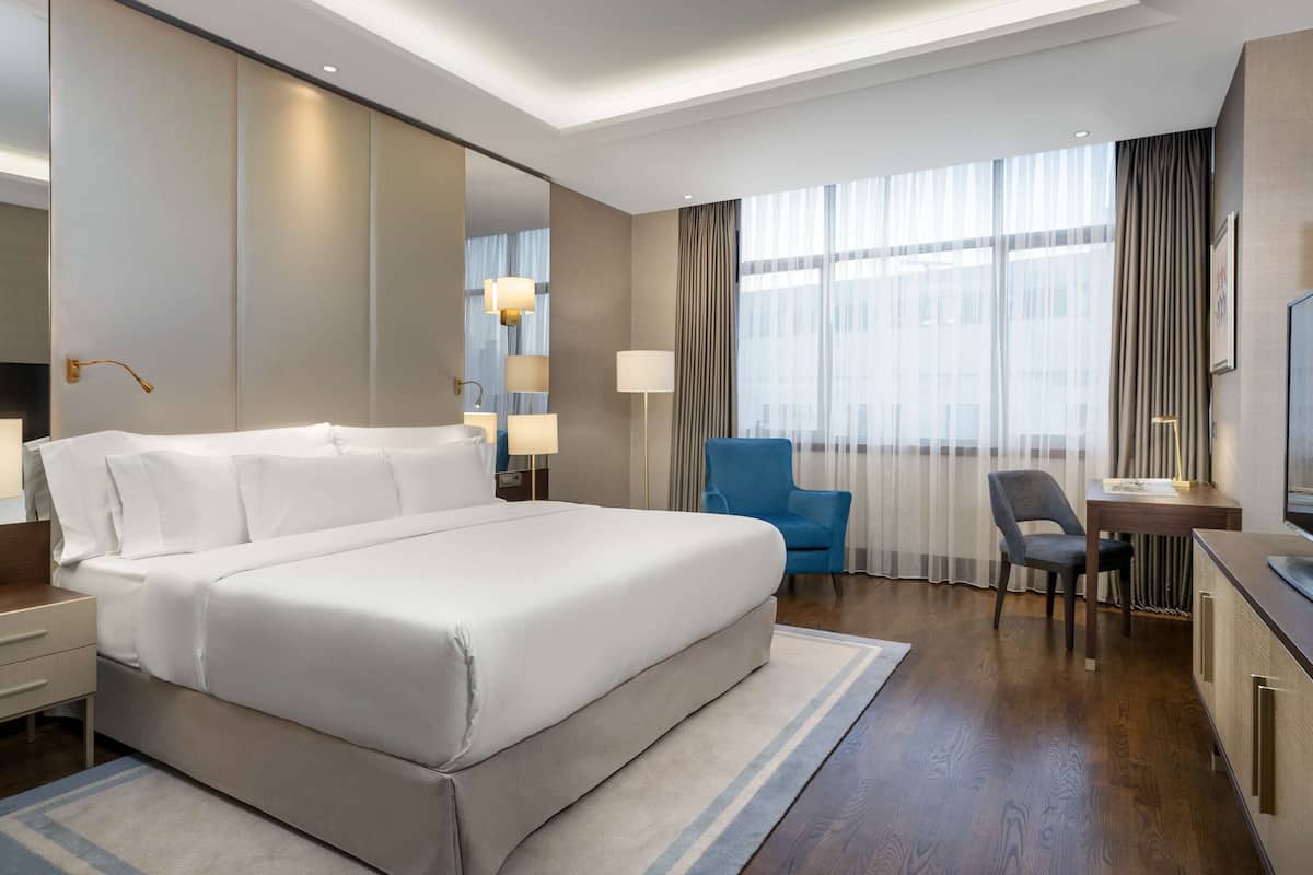 A modern hotel room with a large bed, a desk, a chair, and a TV.