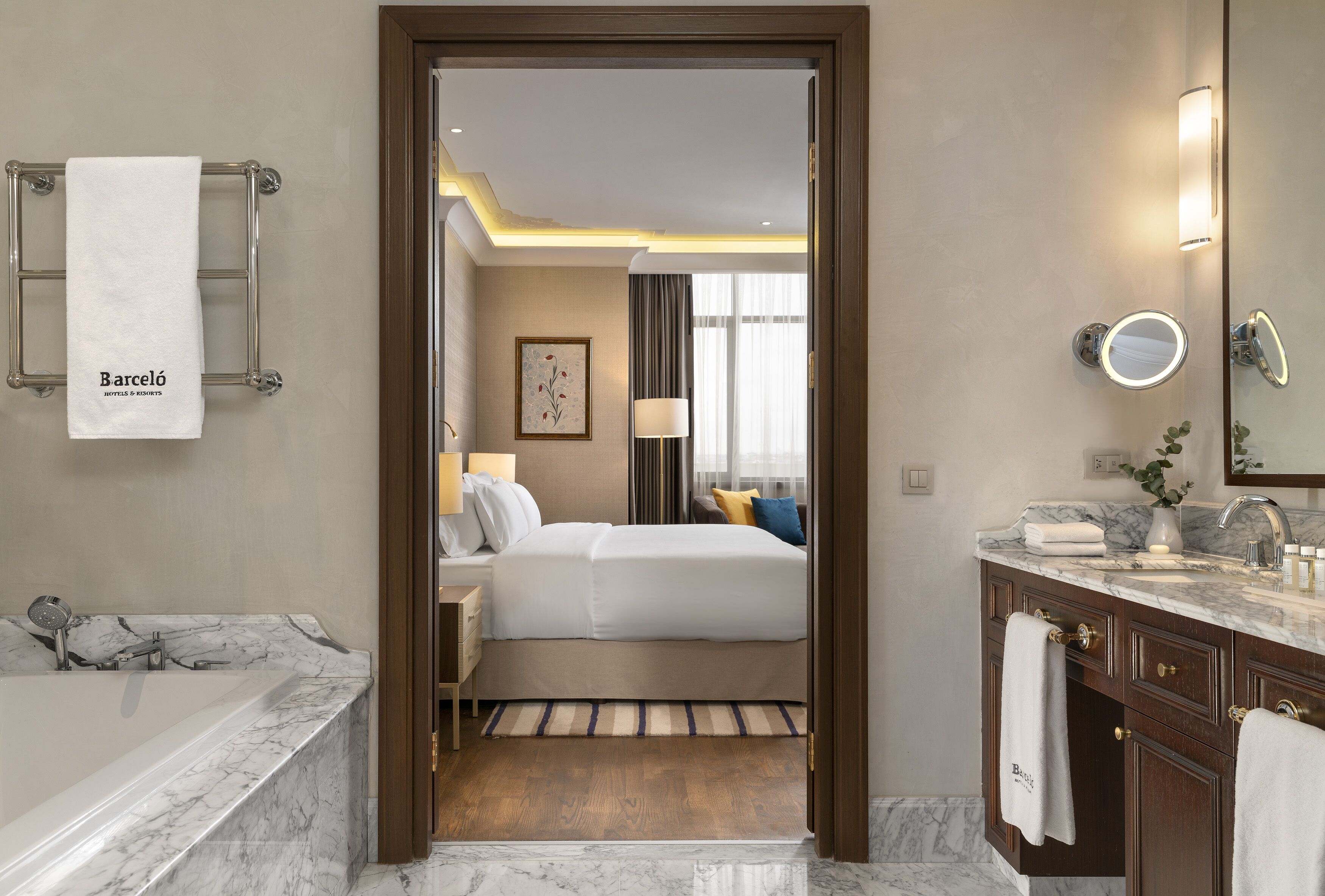 Camera d'albergo con vasca in marmo, un letto con biancheria bianca, un comodino con una lampada e un bagno con lavabo e specchio in marmo.