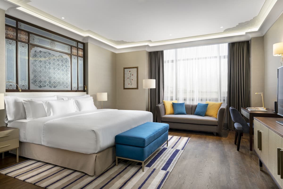 A hotel room with a large bed, a sofa, a desk, and a television.