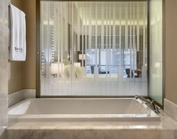 A modern bathroom with a large bathtub, frosted glass window, and a towel hanging on the wall.