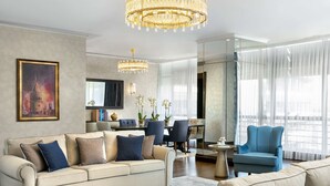 Una sala moderna con un sofá color crema, un sillón azul y una zona de comedor con separador de vidrio.