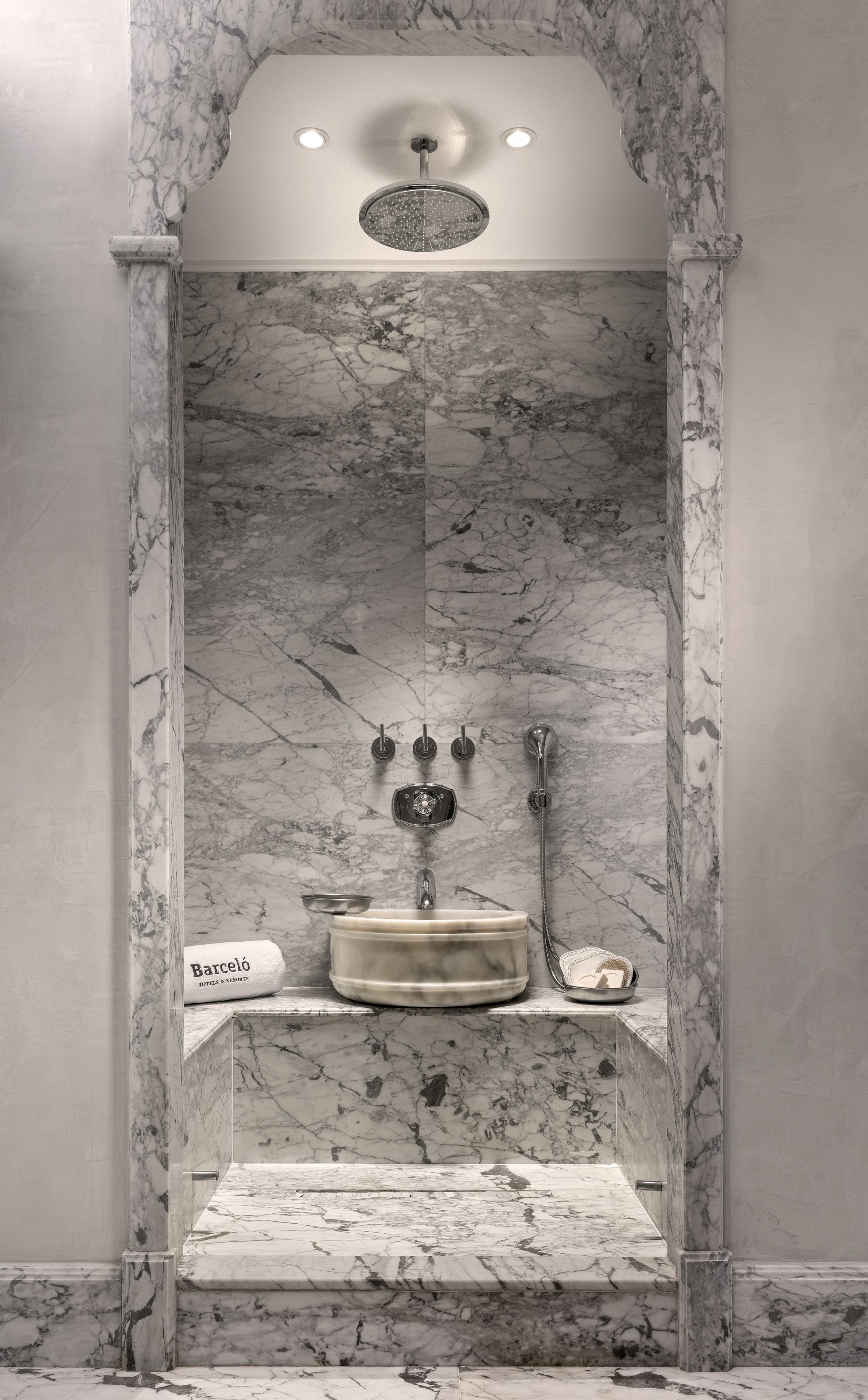 A marble-enclosed shower with a built-in sink, a towel, and a showerhead.