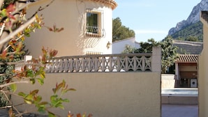 A building with a tiled roof, a window with metal bars, and a stone-paved courtyard. - 0538 Villa Efaistos en el Montgo (Denia)