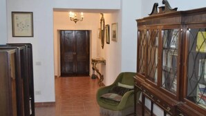 Un couloir avec une porte en bois, un fauteuil vert, une vitrine et un luminaire fixé au mur.