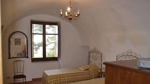 Une chambre avec deux lits, une commode en bois, une chaise, une fenêtre donnant sur un beau paysage et un lustre.
