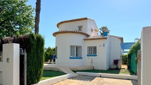 Edifici de color blanc amb detalls blaus i teulada de teules, envoltat de vegetació i un camí empedrat.