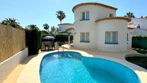 Una piscina amb vora corba, envoltada per un edifici blanc amb detalls blaus i finestres.