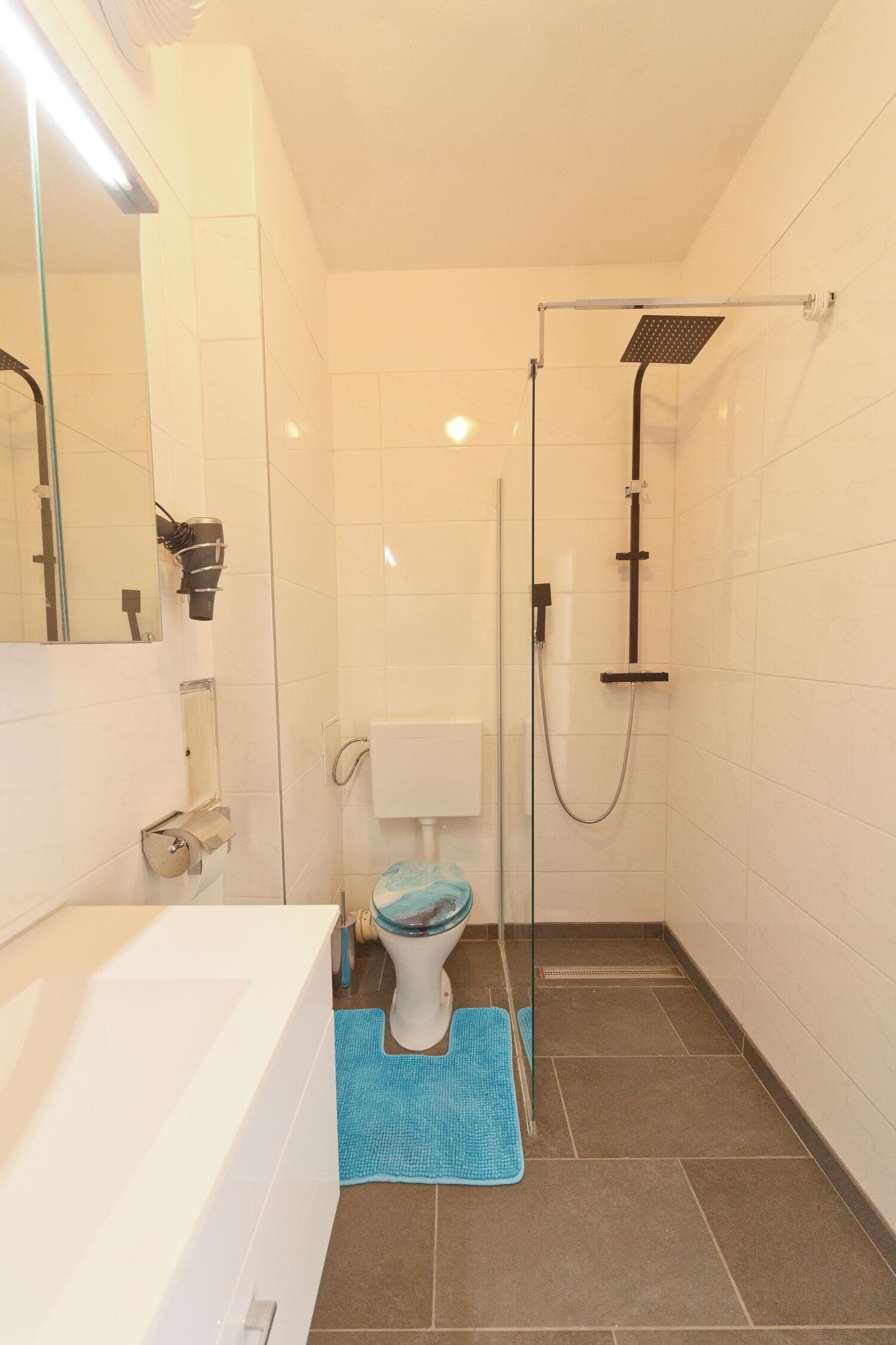 A bathroom with a white toilet, a shower with a glass door, and a blue bath mat.