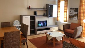 Una sala de estar con televisor, sofá, sillas, una mesita y un aparador.