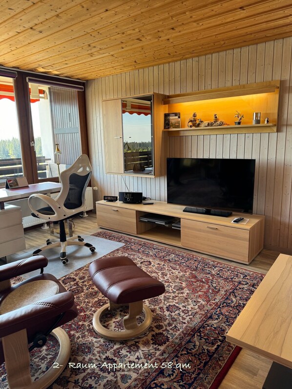 Apartamento de dos ambientes con televisión, muebles de madera, un escritorio y una silla.
