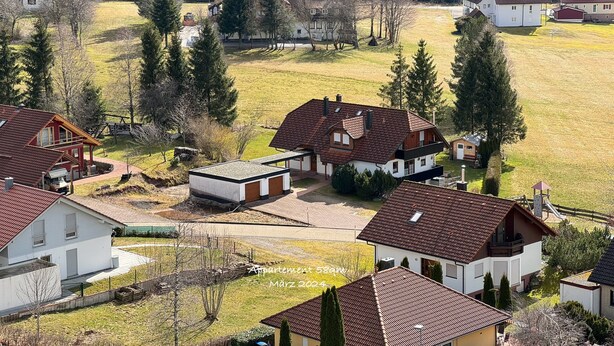 Et boligområde med huse, en legeplads og skov i baggrunden.