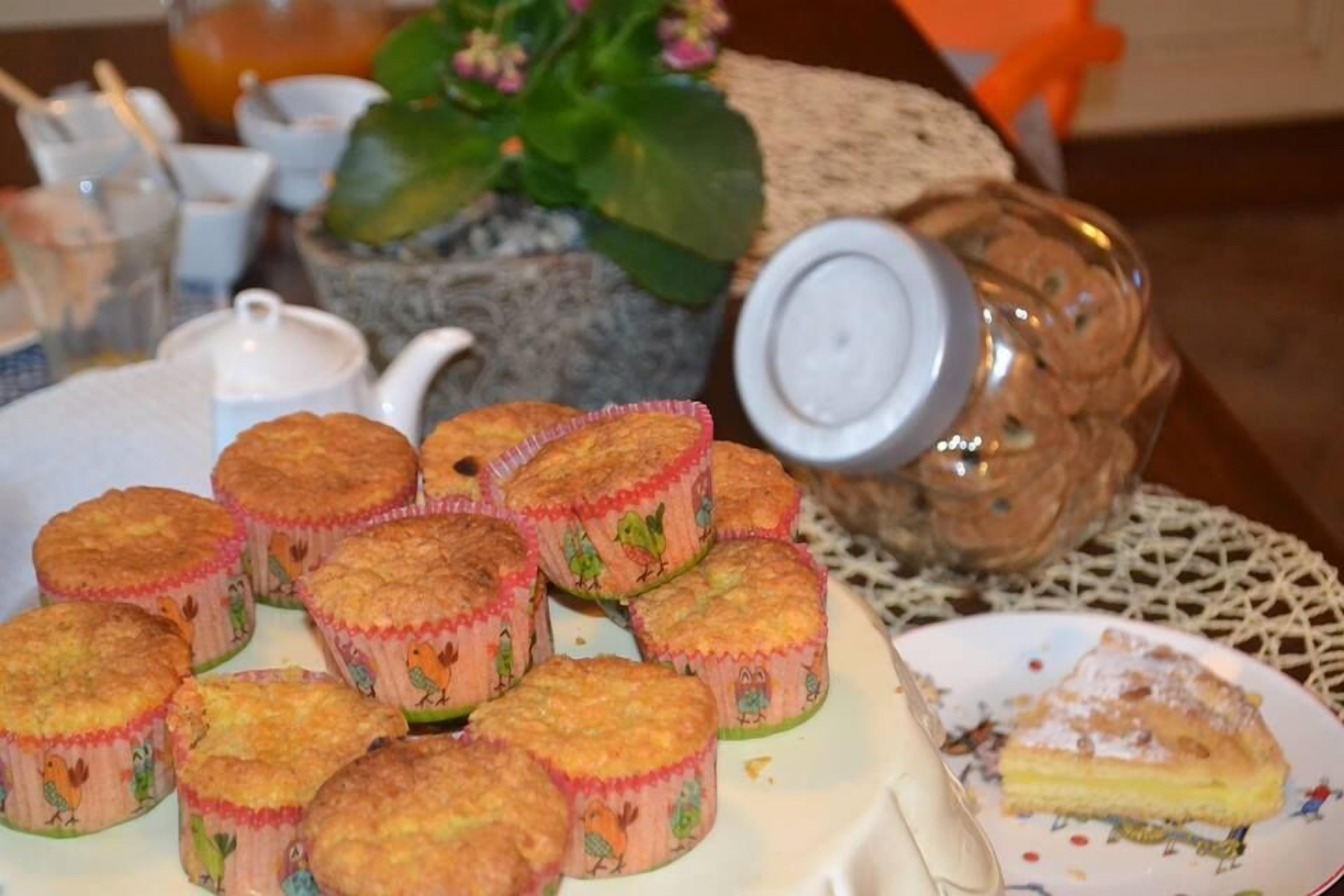 A table with muffins in colorful paper cups, a teapot, and a plate with a slice of pie.