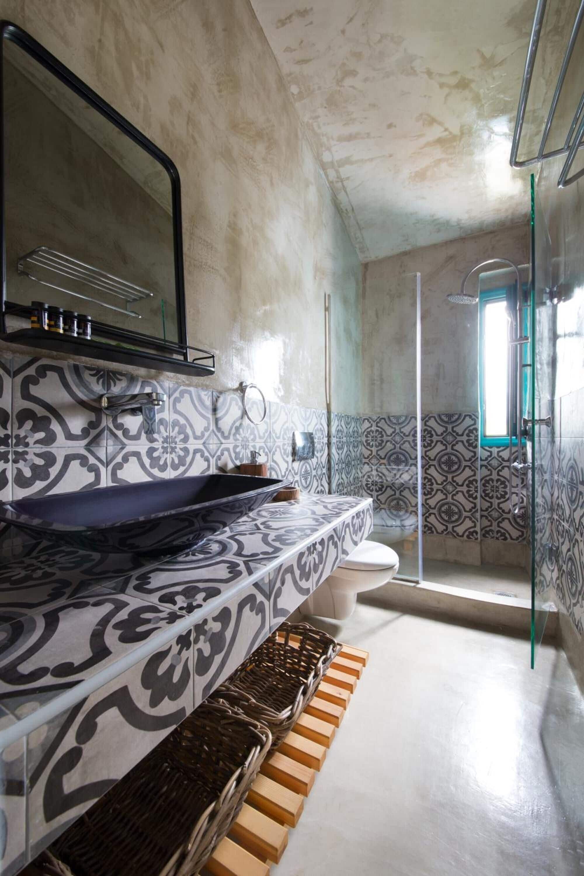 Un baño con un lavabo de diseño, un espejo y baldosas estampadas.