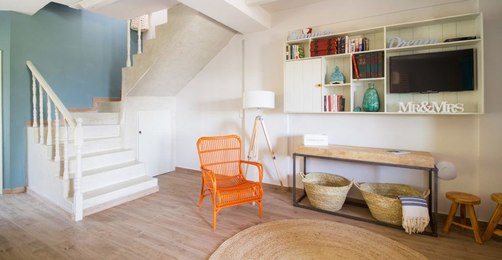 A staircase leading to an upper floor, a wicker chair, a wooden bench, and a bookshelf with books and decorative items.